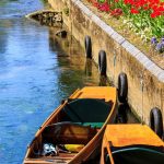 Boats by a flower-lined riverbank.