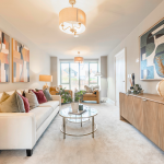 Modern large living room with stylish decor featuring neutral furniture tones with vibrant accents in artwork and cushions. Large window bringing in natural light at Avon Bard in Stratford Upon Avon.